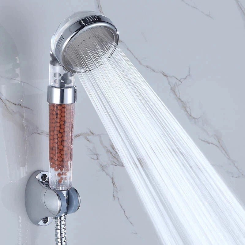 Chrome shower head spraying a strong stream; amber bead filter column visible